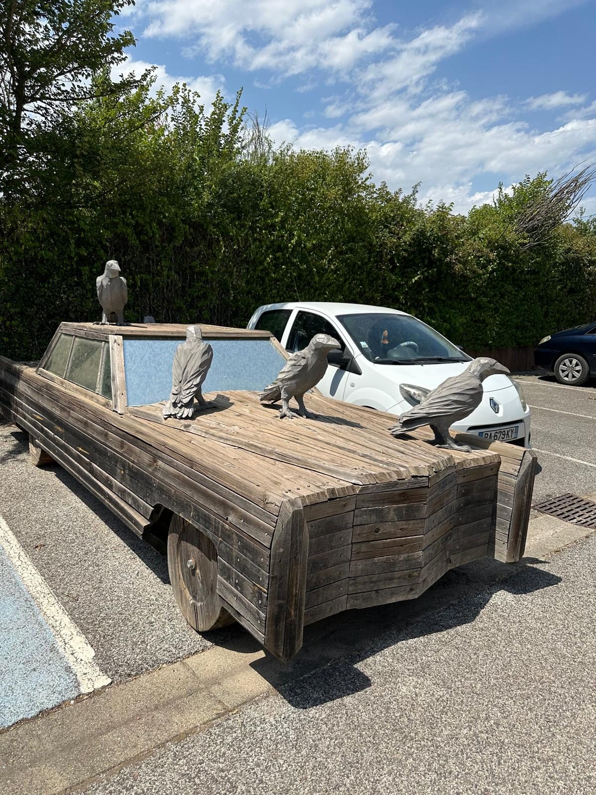 In the forecourt: a full-size Cadillac built entirely from timber, carrying a parliament of carved crows.